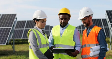 Portrait of electrician engineers in safety helmet and uniform checking solar panels. Group of...