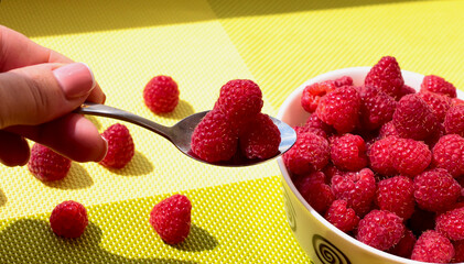 Ripe raspberries on a spoon. Raspberries in a white plate on a green table.