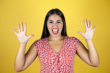 Young beautiful woman over isolated yellow background showing and pointing up with fingers number ten while smiling confident and happy