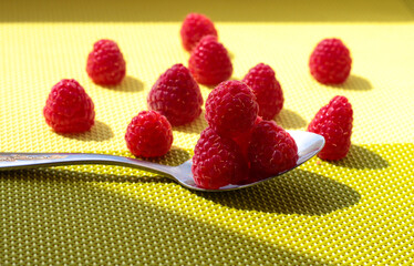 Ripe raspberries on a spoon. Raspberries in a white plate on a green table.