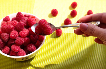Ripe raspberries on a spoon. Raspberries in a white plate on a green table.