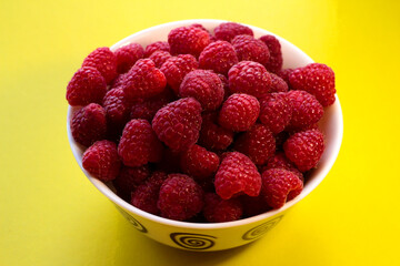 Raspberries in a white plate on a yellow background.