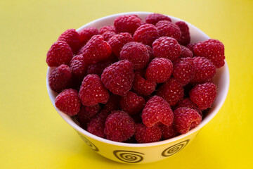 Raspberries in a white plate on a yellow background.