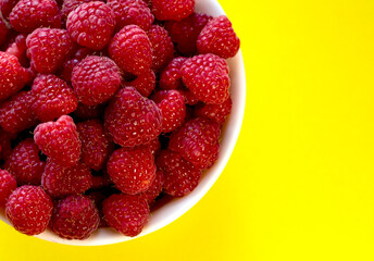 Raspberries in a white plate on a yellow background.