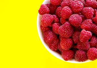 Raspberries in a white plate on a yellow background.