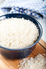 Uncooked basmati rice in a ceramic bowl on wooden background