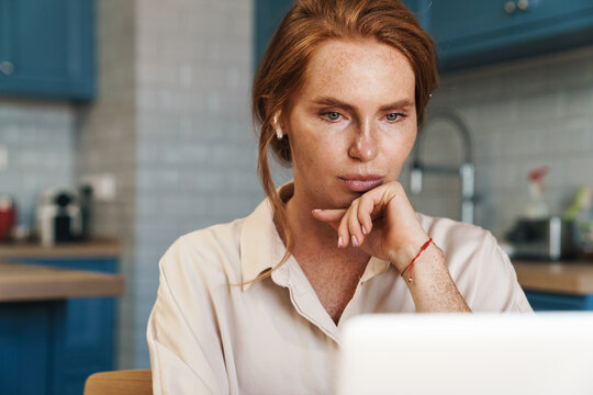 Image of serious ginger woman in earphones working with laptop