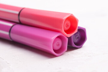 three markers or pens in pink, purple, pink on a white concrete background, slide or pile.