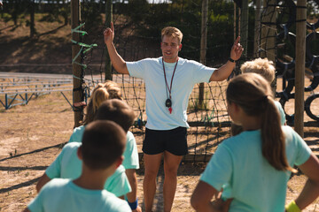 Male fitness coach instructing while kids at a boot camp