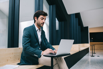 Serious Indian man working with information database on modern laptop computer connecting to...