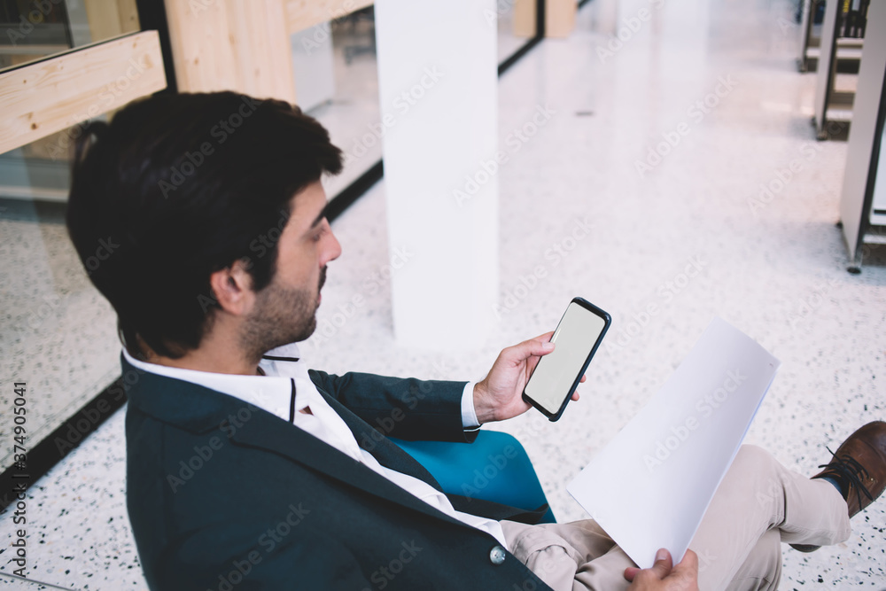 Poster male employee reading corporate report and using mockup cellphone technology during working process,