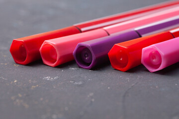 five markers or pens in pink, purple, pink on a black background.