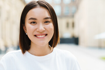 Positive young asian woman walking by street outdoors