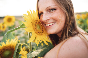 Close up portrait of smiling young woman with fresh yellow sunflower at farm