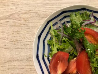 木目のテーブルに置かれたトマトとルッコラと玉ねぎとわさび菜のサラダ