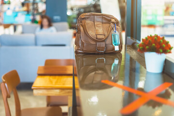 Mini portable alcohol gel bottle to kill Corona Virus(Covid-19) hang on a brown leather shoulder bag on counter in coffee shop.New normal lifestyle. Health care concept. Selective focus on alcohol gel