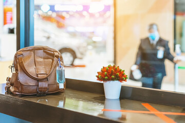 Mini portable alcohol gel bottle to kill Corona Virus(Covid-19) hang on a brown leather shoulder bag on counter in coffee shop.New normal lifestyle. Health care concept. Selective focus on alcohol gel