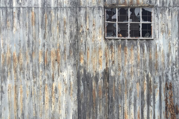 A picturesque weathered corrugated iron wall of a shed with a window with broken panes