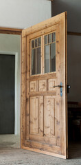 An old box-wood door with windows of untreated spruce wood stands open into a room.