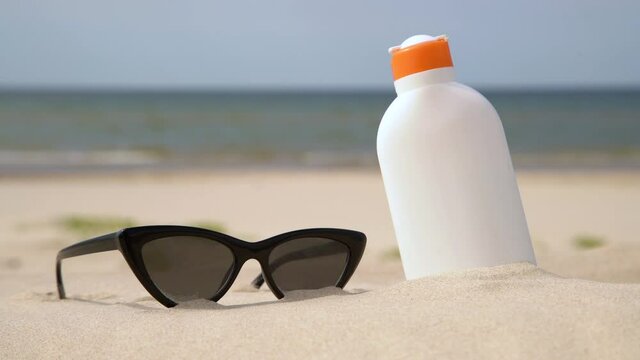 Sunscreen protection lotion and sunglasses in the sand on a sunny day at the beach. White sunblock cream protection bottle from sunburn. Nobody.