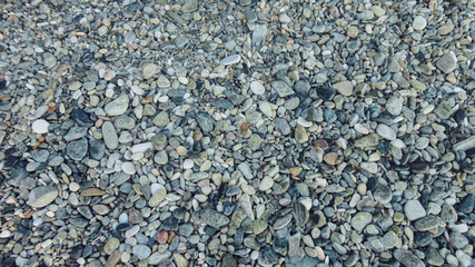 Stony beach on a sunny day. Background of different pebbles from above on the beach