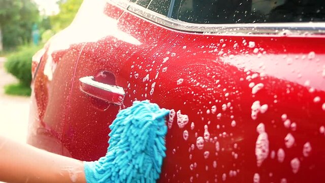 Close up of hand is washing car by mitt with bubbles soap outdoors.