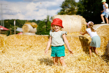 Little toddler girl having fun with running and jumping on hay stack or bale. Funny happy healthy...