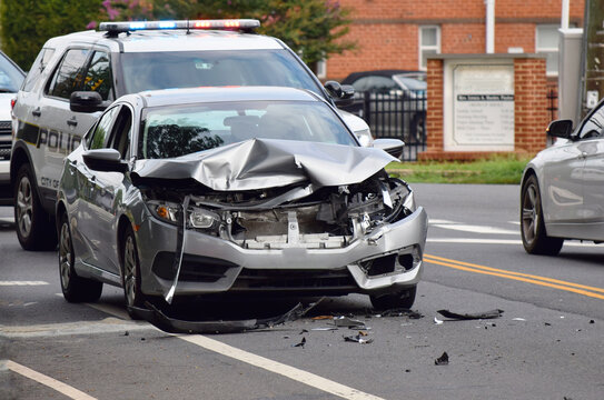 Front photo of a traffic accident. Car in a collision with front smashed and destroyed, debris on road and police car in background.