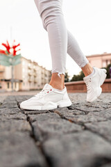 Woman in fashionable casual white clothes and shoes on a walk in the city. Close-up.