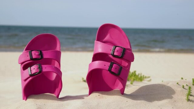 Pink sandals at the beach on a beautiful sunny day. Slippers in the sand by the sea. Flip flops at the shore by the ocean.