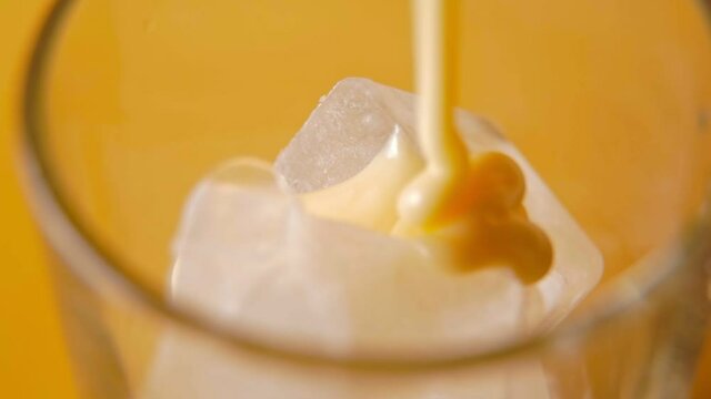 Pouring condensed milk on ice closeup - yellow background