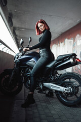 Redhead sexy female biker rides her modern motorcycle