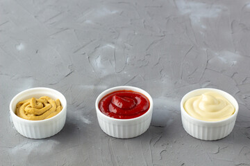 Set of three kinds of classic sauces on gray stone background. Mayonnaise ketchup mustard