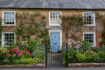 The exterior of an english cottage with flowers blooming in the front garden and sash windows, A...