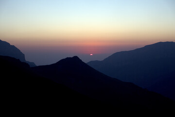 Silhouettes of mountains in the morning haze. The sun rises over the mountains.