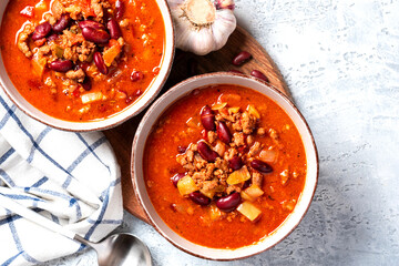 Chili con carne in a bowl on a grey concrete background top view. Tex-mex food. Delicious spicy soup with red beans, peppers, tomatoes and minced meat. Copy space
