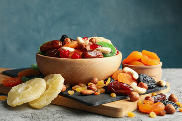Board and bowls with dried fruits and nuts on gray background