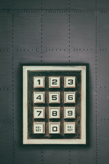 Vintage weathered keypad with reset and number buttons on a dark grey wall