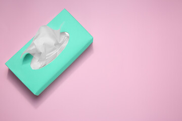 Box with paper tissues on pink background, top view. Space for text