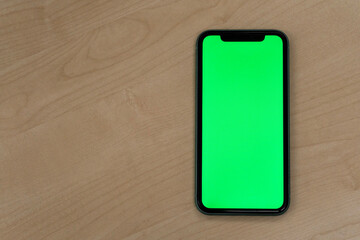 top view of one green screen smart phone on patterned wooden table.