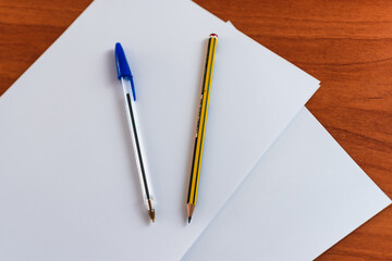 A pen and pencil on two white papers with a wooden table in the background