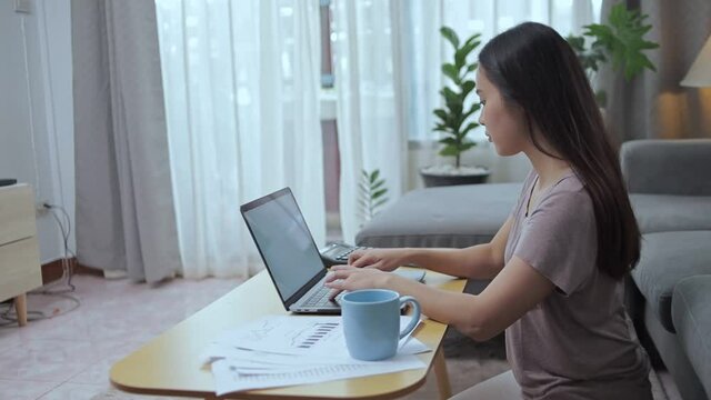 woman busy working on laptop and use mobile phone for talking with customer and short note in a book at home.