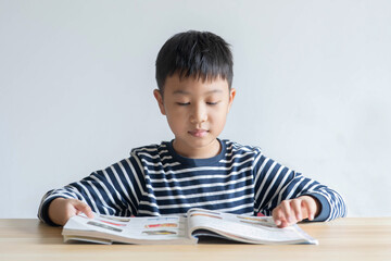 Asian boy who are studying in elementary school reading and doing homework by himself at home.