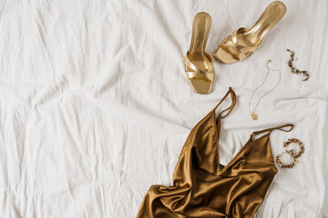 Sexy fashion concept with women's clothes and accessories. Golden shoes, brown silk dress, golden...