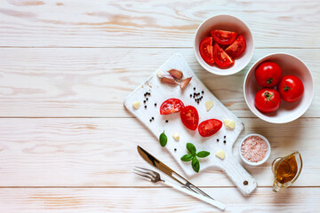 Beautiful fresh raw tomatoes with olive oil, greens and spices. Top view, close-up on white wooden background