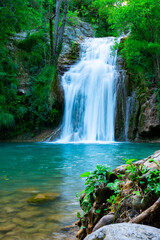 A large beautiful waterfall in a forest with blue water and a trees.