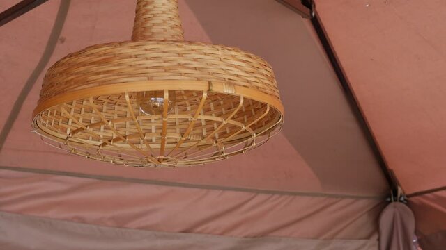 A light bulb in a wicker lampshade against the background of a fabric awning in a street cafe. Retro style. Vintage interior. The chandelier sways in a gentle breeze. Soft beige coffee pastel colors