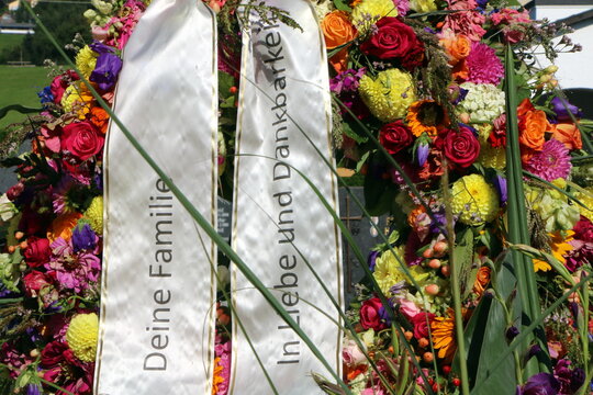 Blumenkranz am Friedhof nach einer christlichen Beisetzung in &Ouml;sterreich, Trauerb&auml;nder in deutscher Sprache an einem Grab "In Liebe und Dankbarkeit - Deine Familie", bunter Blumenschmuck am Grab