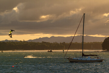 Harbor at sunset. A sailboat and a kite surfer are on the water. Mount Maunganui, New Zealand