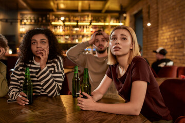 Friends looking disappointed while watching sports match on TV together, drinking beer and cheering for team in the bar. People, leisure, friendship and entertainment concept
